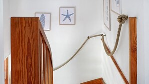 Una escalera de madera con una cuerda atada al barandal, una estrella de mar enmarcada y una pared blanca.