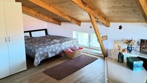 Een slaapkamer met een bed, een kledingkast, een raam, een houten plafond en een kleine tafel met decoratieve objecten.