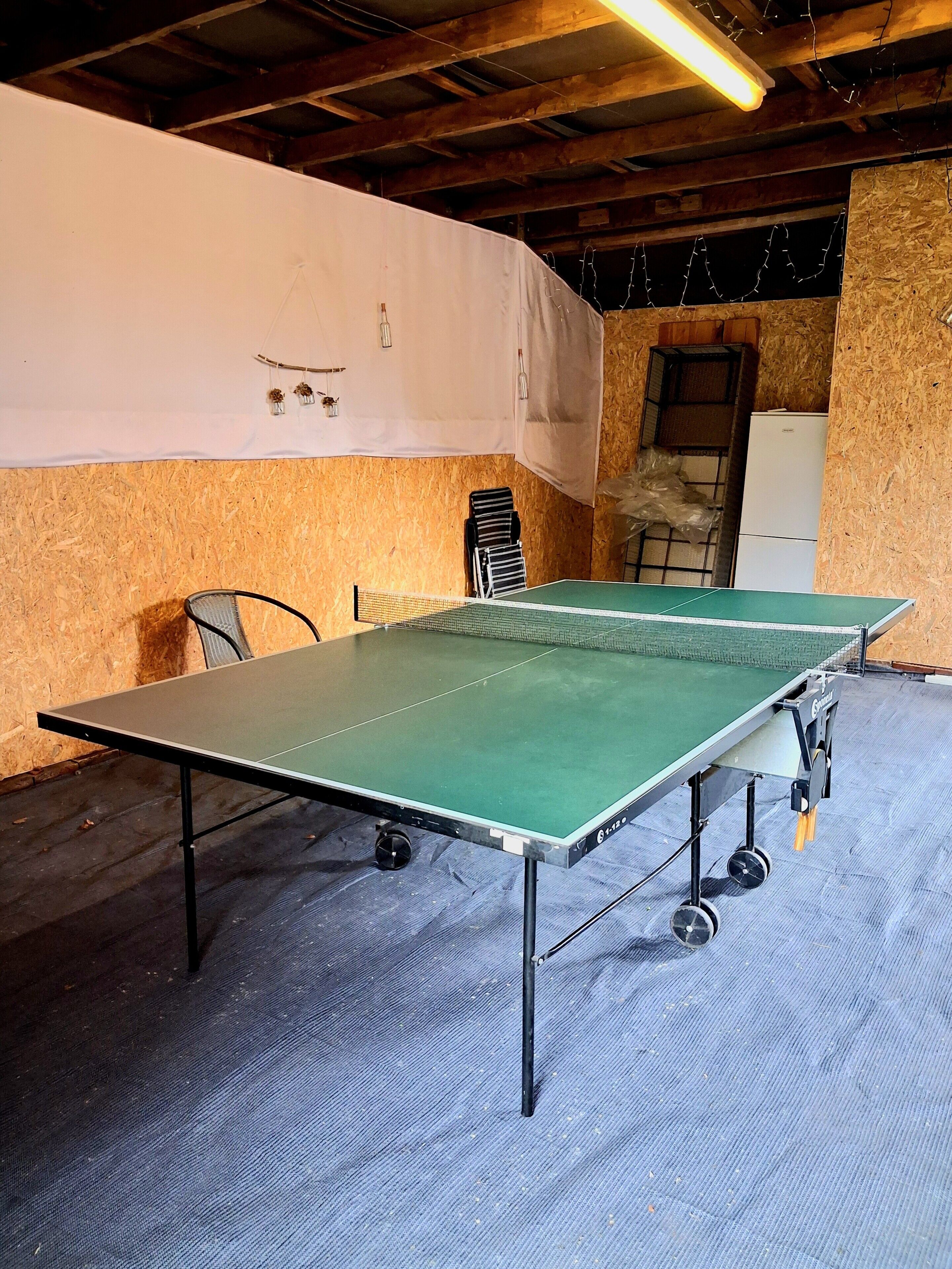 Une table de ping-pong dans une pièce aux murs en bois et dotée d’un ventilateur de plafond.
