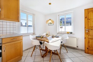 Une cuisine avec des meubles blancs, un plan de travail en bois, une table à manger avec des chaises et un luminaire suspendu.