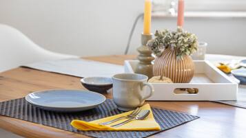 A wooden table with a blue plate, a gray mug, a yellow napkin, and a silver spoon.