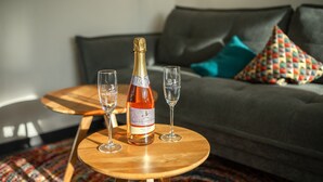 A bottle of wine on a wooden table with two glasses, a grey sofa, and colorful pillows in a living room. - Baßler Schlossblick Apartment with Private Terrace, Balcony and Wi-Fi (Kappelrodeck)