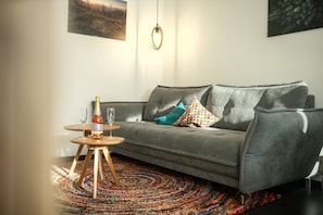 Una sala de estar moderna con un sofá gris, almohadas coloridas, una mesita de madera con vasos y una alfombra llamativa.