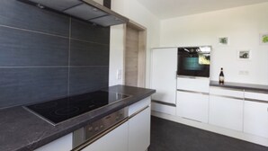 A modern kitchen with a black stovetop, white cabinets, and a built-in oven. - Baßler Schlossblick Apartment with Private Terrace, Balcony and Wi-Fi (Kappelrodeck)