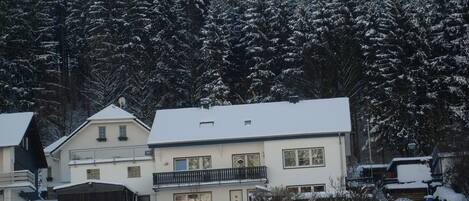 A residential building with a balcony, surrounded by snow-covered trees.