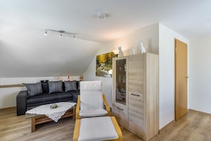 Una sala moderna con un sofá, una mesa de centro de vidrio, una silla blanca, un aparador de madera y una puerta.
