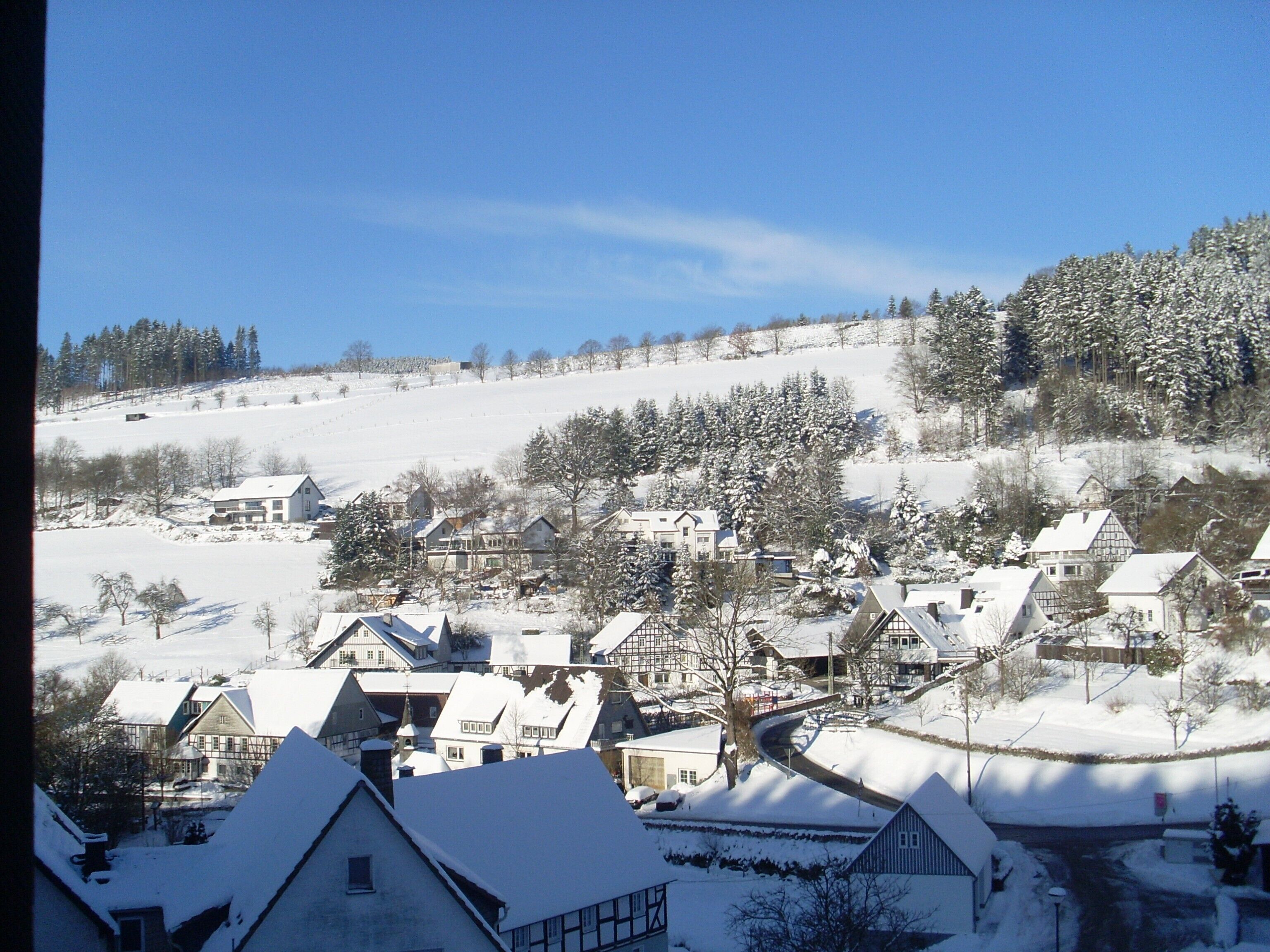 A snow-covered village with traditional houses, a church, and a hill in the background.