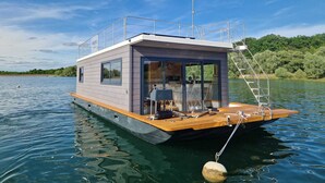 Een drijvend woonschip met een overdekt terras, een klein keukentje en een badkamer.