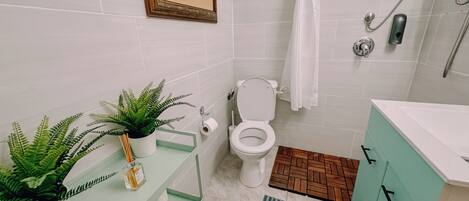 A bathroom with a toilet, a sink with a mirror, a shower area, and a small potted plant.