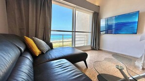 Un salón moderno con un sofá de cuero, una mesa de centro de vidrio y un televisor grande en la pared.