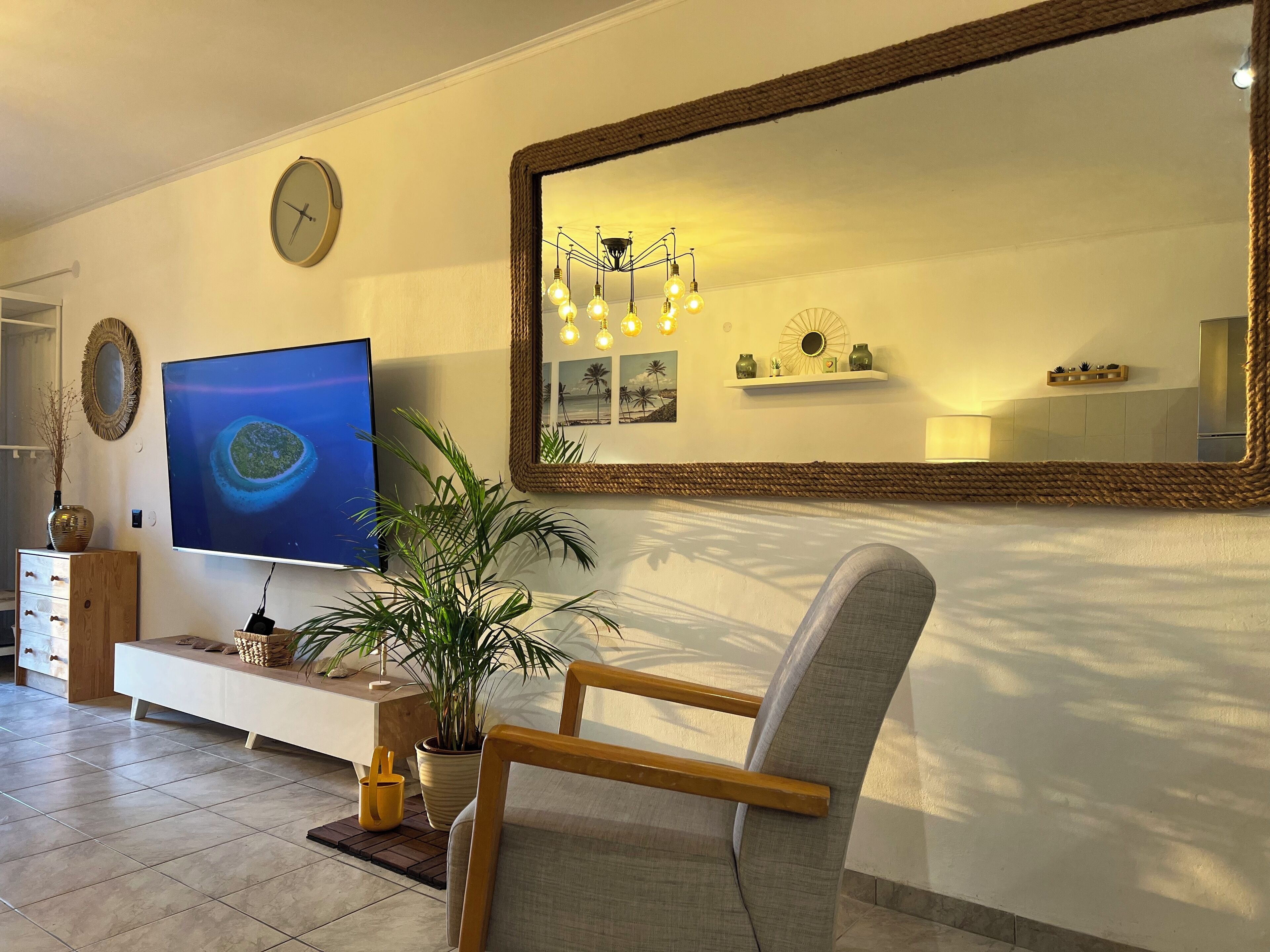 A living room with a television, a large mirror, a plant, and a chair.