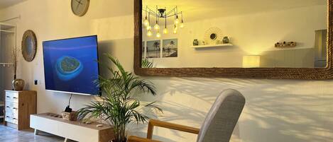 A living room with a television, a large mirror, a plant, and a chair.