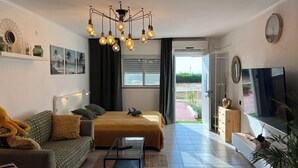 Una sala de estar moderna con cama, sofá, televisor y un amplio ventanal.