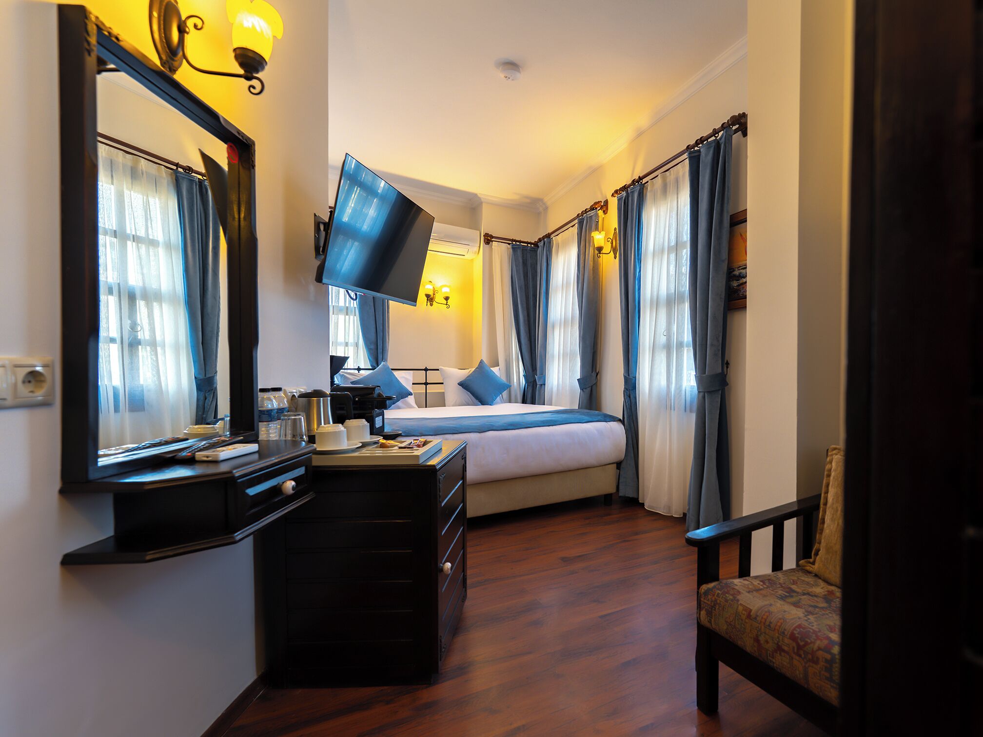 A hotel room with a bed, a desk with a flat-screen TV, a chair, and a dresser.