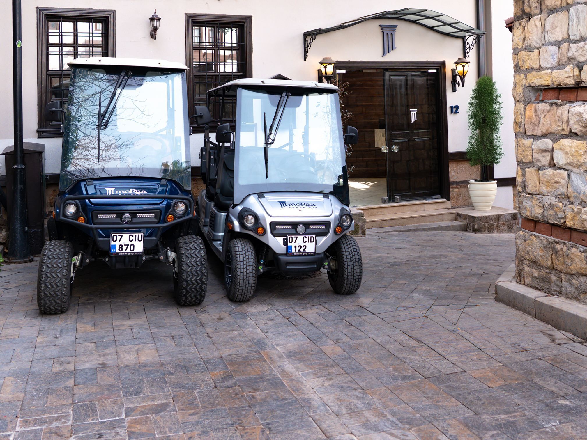 Dos carritos de golf estacionados frente a un edificio con paredes de piedra y una puerta grande de madera.