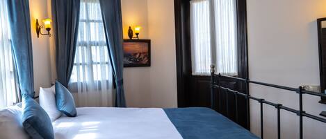 A hotel room with a bed, curtains, a painting, and a door.