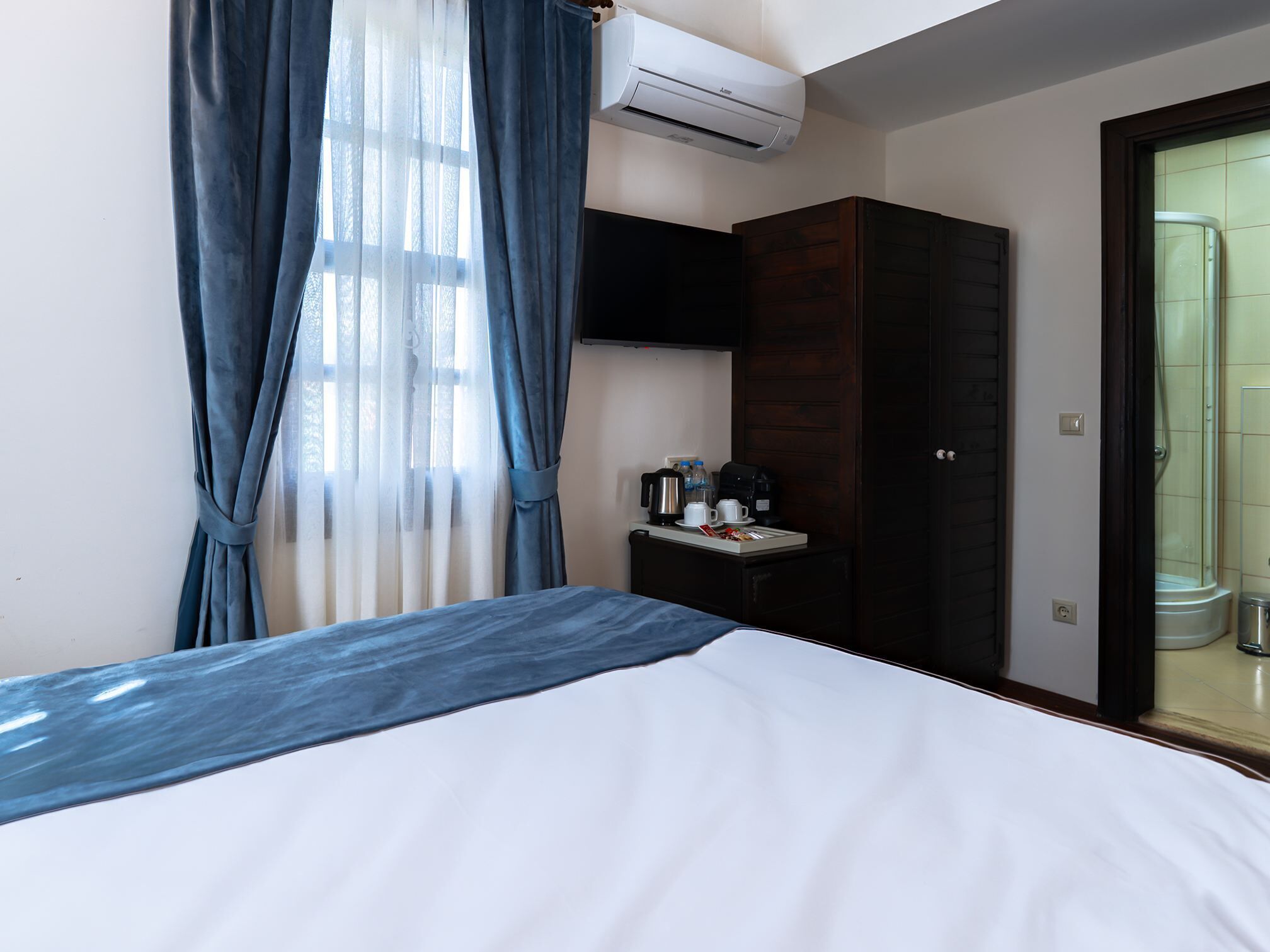 A hotel room with a bed, a small table with a coffee maker, a wardrobe, and a shower area.
