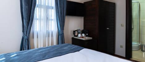 A hotel room with a bed, a small table with a coffee maker, a wardrobe, and a shower area.