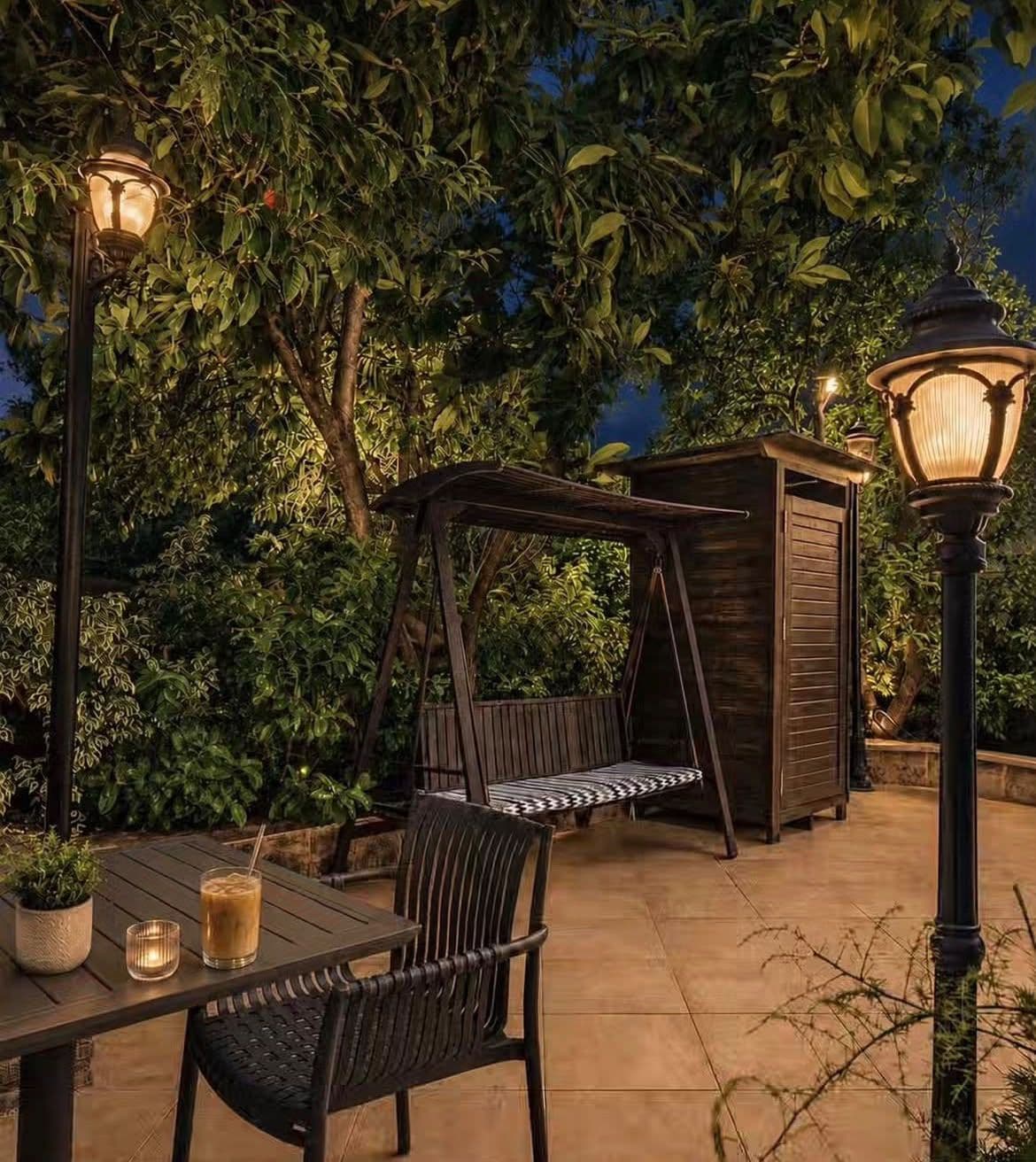 An outdoor patio with a swing chair, a table with a drink, and a lamp post.