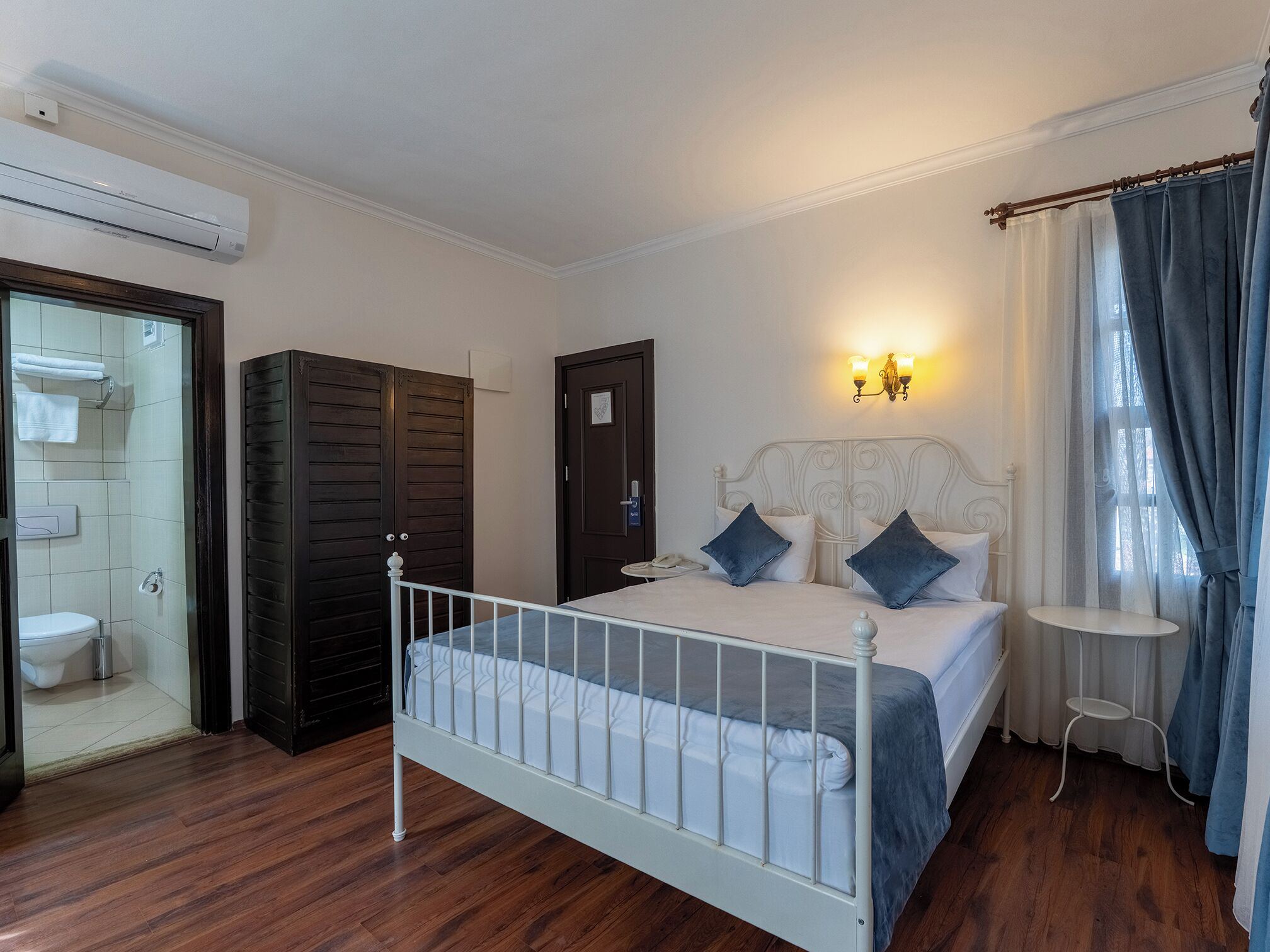 A bedroom with a bed, a bedside table, a wardrobe, a bathroom with a toilet, and an air conditioning unit.