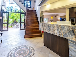 Vestíbulo de hotel con mostrador de recepción de mármol, una escalera de madera y vistas al exterior.