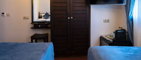 A hotel room with two beds, a TV, a wardrobe, and a small table with a kettle.