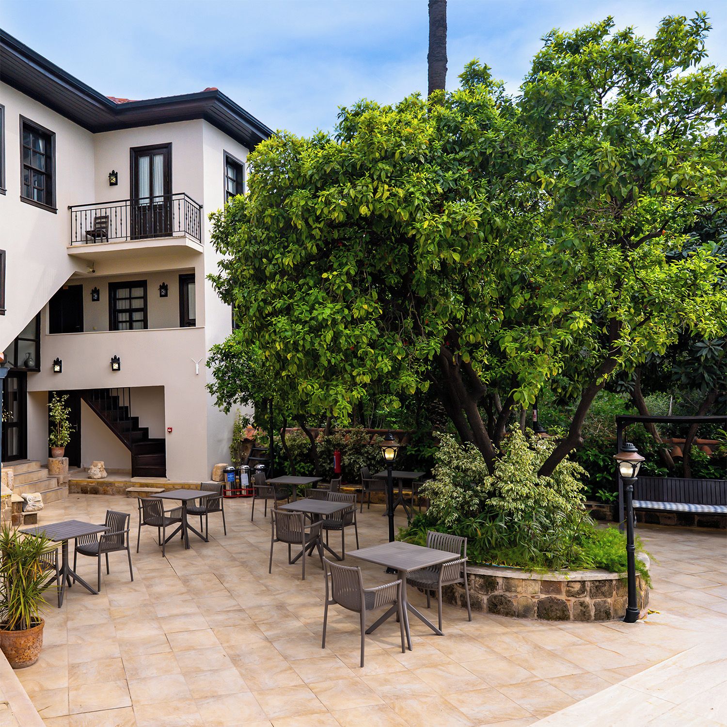 Un patio con mobiliario exterior, una escalera y un edificio con balcón.