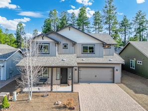 A two-story house with a garage, a front porch, and a small yard with a tree and gravel.