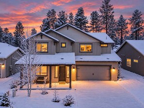 Ein zweistöckiges Haus mit Garage, umgeben von schneebedeckten Bäumen und einer Auffahrt.