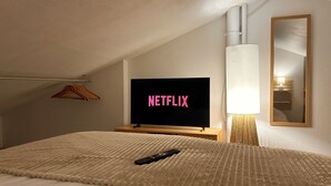 A hotel room with a bed, a TV displaying the Netflix logo, a remote control, a lamp, and a mirror on the wall. - L'Atlantide Maison & Spa - Direct access to the beach (Saint-Hilaire-de-Riez)