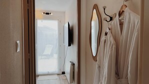 A hallway with a door leading to a balcony, a wall-mounted TV, and a towel rack with a robe. - L'Atlantide Maison & Spa - Direct access to the beach (Saint-Hilaire-de-Riez)