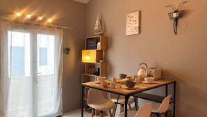 A dining area with a table set for four, a bookshelf, a wall-mounted bicycle light, and a window with curtains. - L'Atlantide Maison & Spa - Direct access to the beach (Saint-Hilaire-de-Riez)