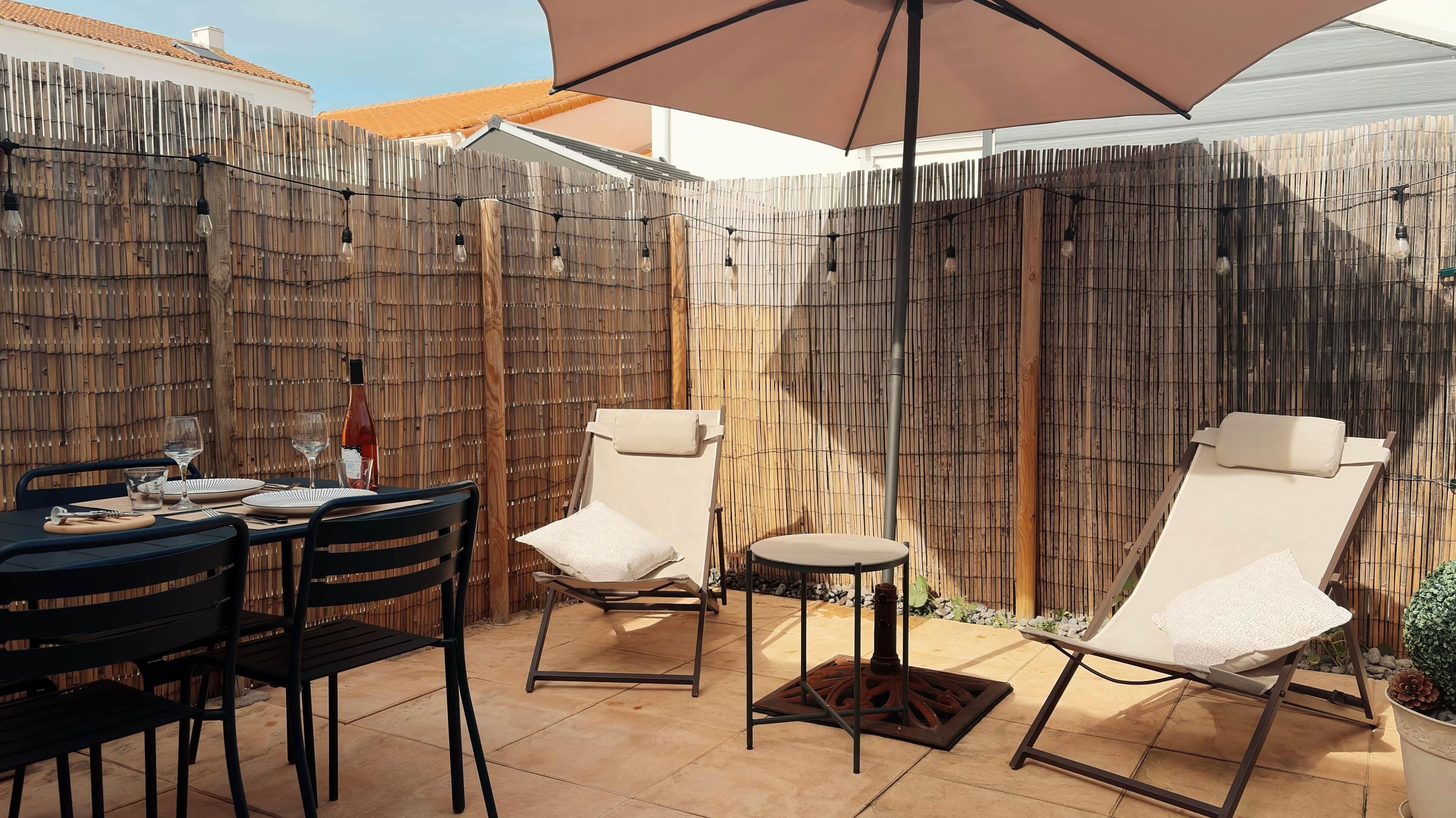 Eine Terrasse im Freien mit Esstisch, zwei Lounge-Stühlen und einem dekorativen Zaun.