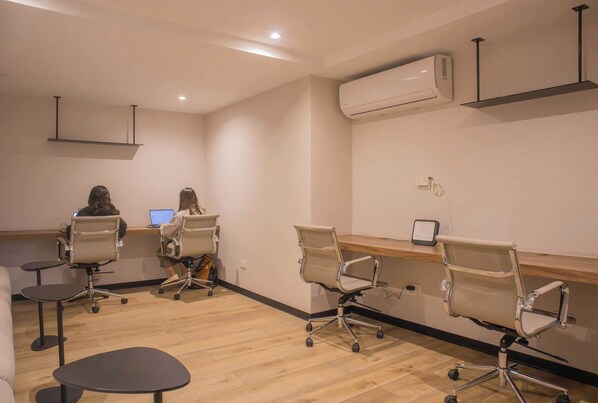 A modern office space with two people working at desks, a standing desk, and an air conditioning unit on the wall.
