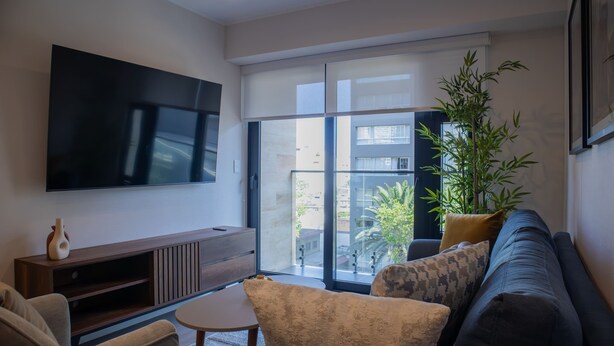 Una sala de estar moderna con un televisor de pantalla plana grande montado en la pared, un sofá, una mesa de centro y una planta en maceta.