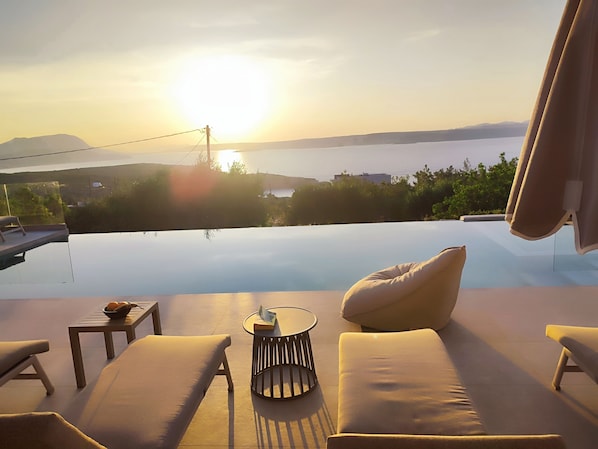 A sunlit outdoor seating area with a view of the sea and mountains.