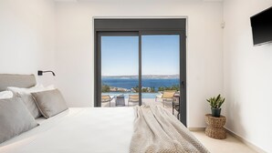 A bedroom with a bed, a view of the sea, and a balcony with chairs. - Brand new 2025,  villa Cactus by NiMaR villas, stunning seaviews infinity pool (kokkino chorio)