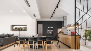 A modern kitchen with a dining area, featuring a central island, dark cabinetry, and a staircase with a geometric design. - Brand new 2025,  villa Cactus by NiMaR villas, stunning seaviews infinity pool (kokkino chorio)