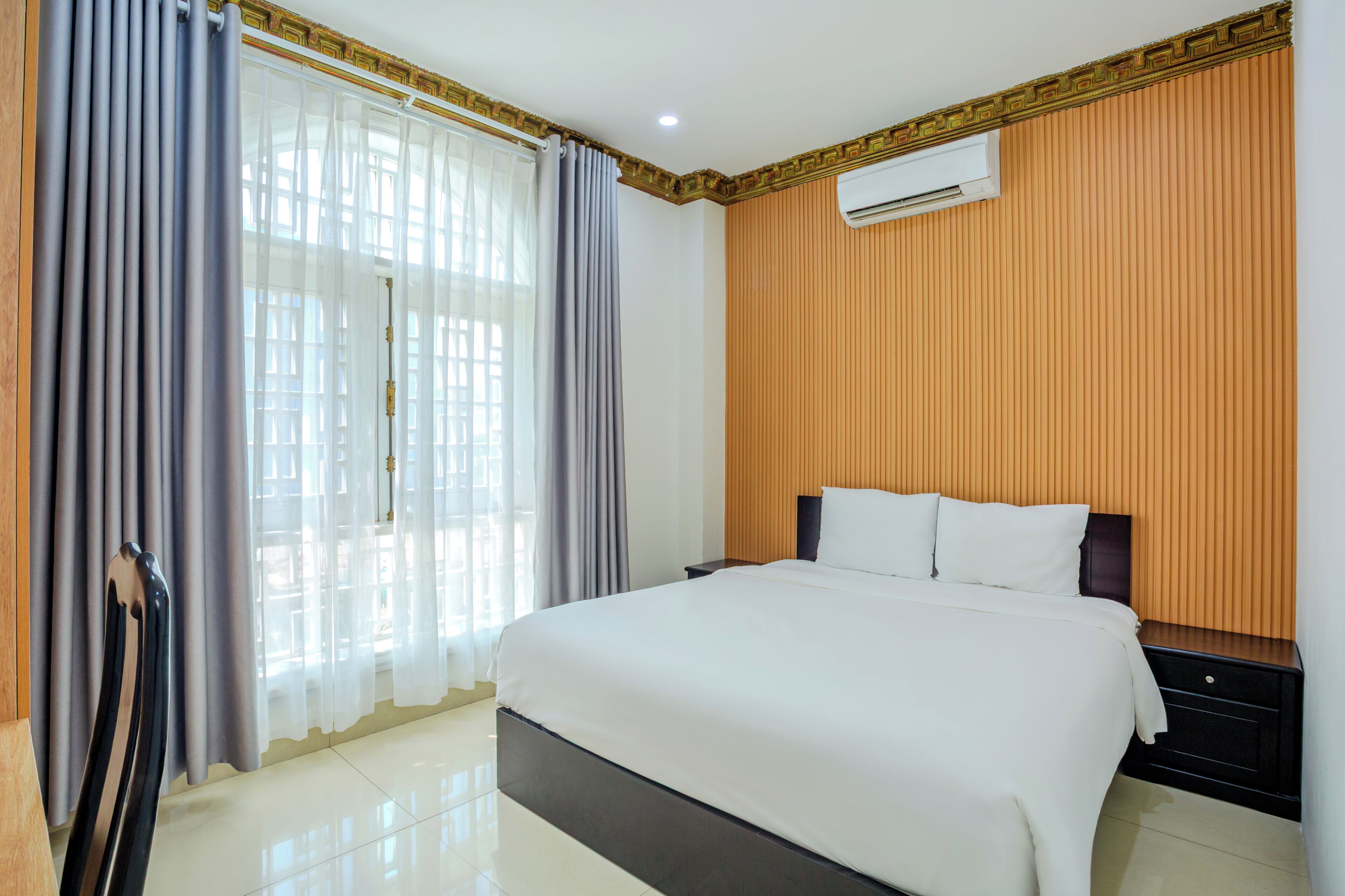 A hotel room with a large bed, a nightstand, a window with curtains, and a wall-mounted air conditioner.