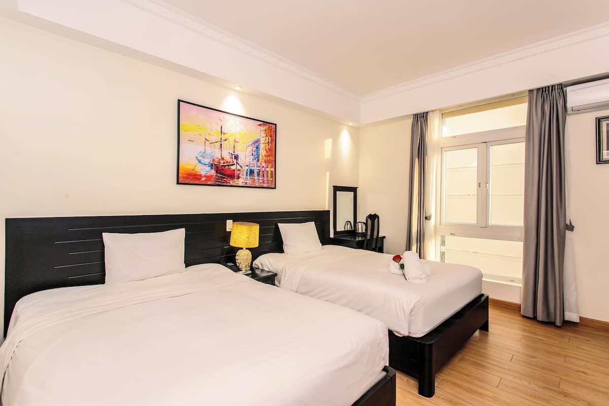 Habitación de hotel con dos camas, un cuadro en la pared, una ventana con cortinas y una mesita de noche con lámpara.
