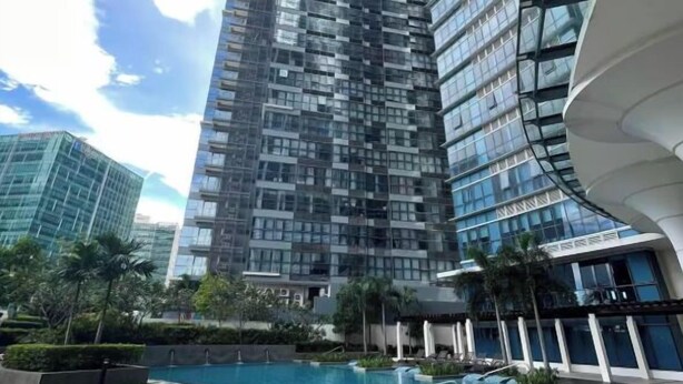 A modern high-rise building with a glass facade, a swimming pool, and a well-maintained lawn. - Luxury Uptown Parksuites - BGC (Taguig)