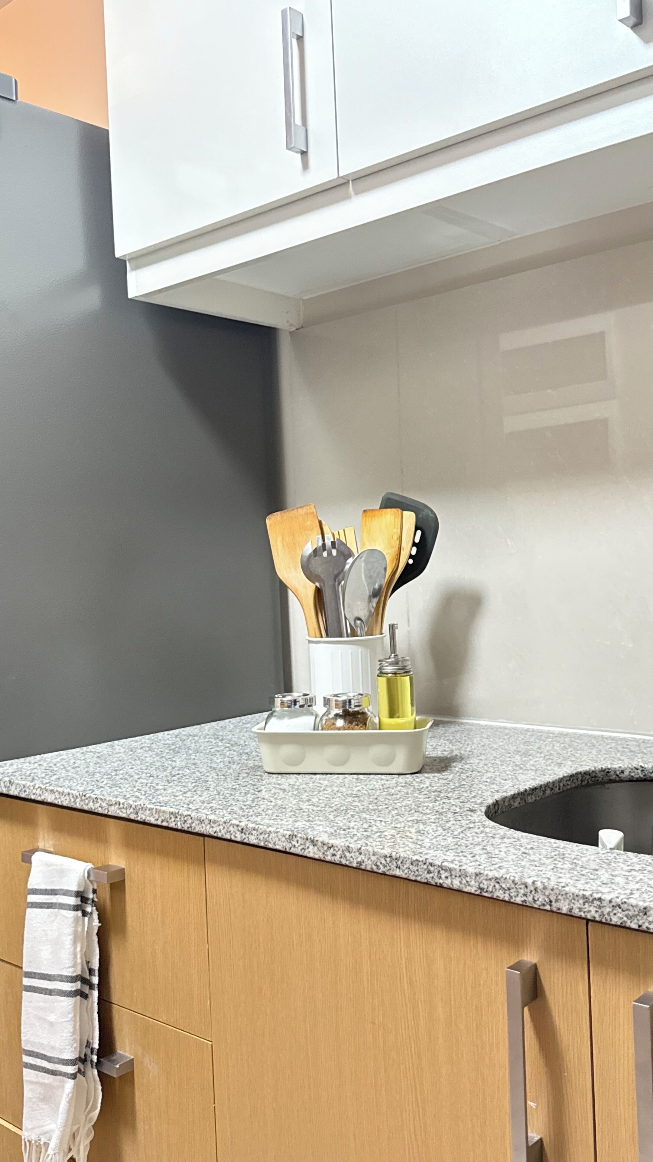 A kitchen with a granite countertop, wooden cabinets, and a utensil holder with wooden and metal utensils.