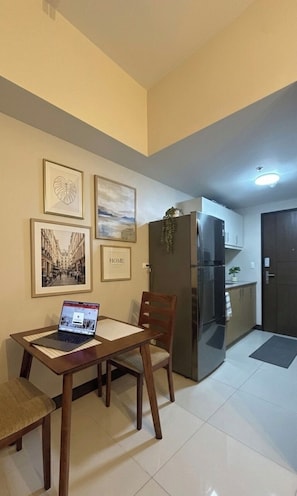 A compact kitchen with a refrigerator, a dining table with chairs, and framed pictures on the wall.