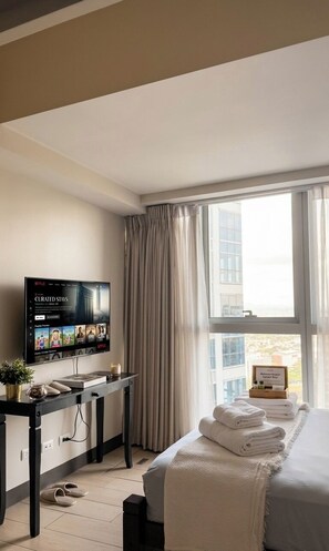 A hotel room with a bed, a TV, a desk, and a window with curtains. - Uptown Parksuites Tower One (Taguig)