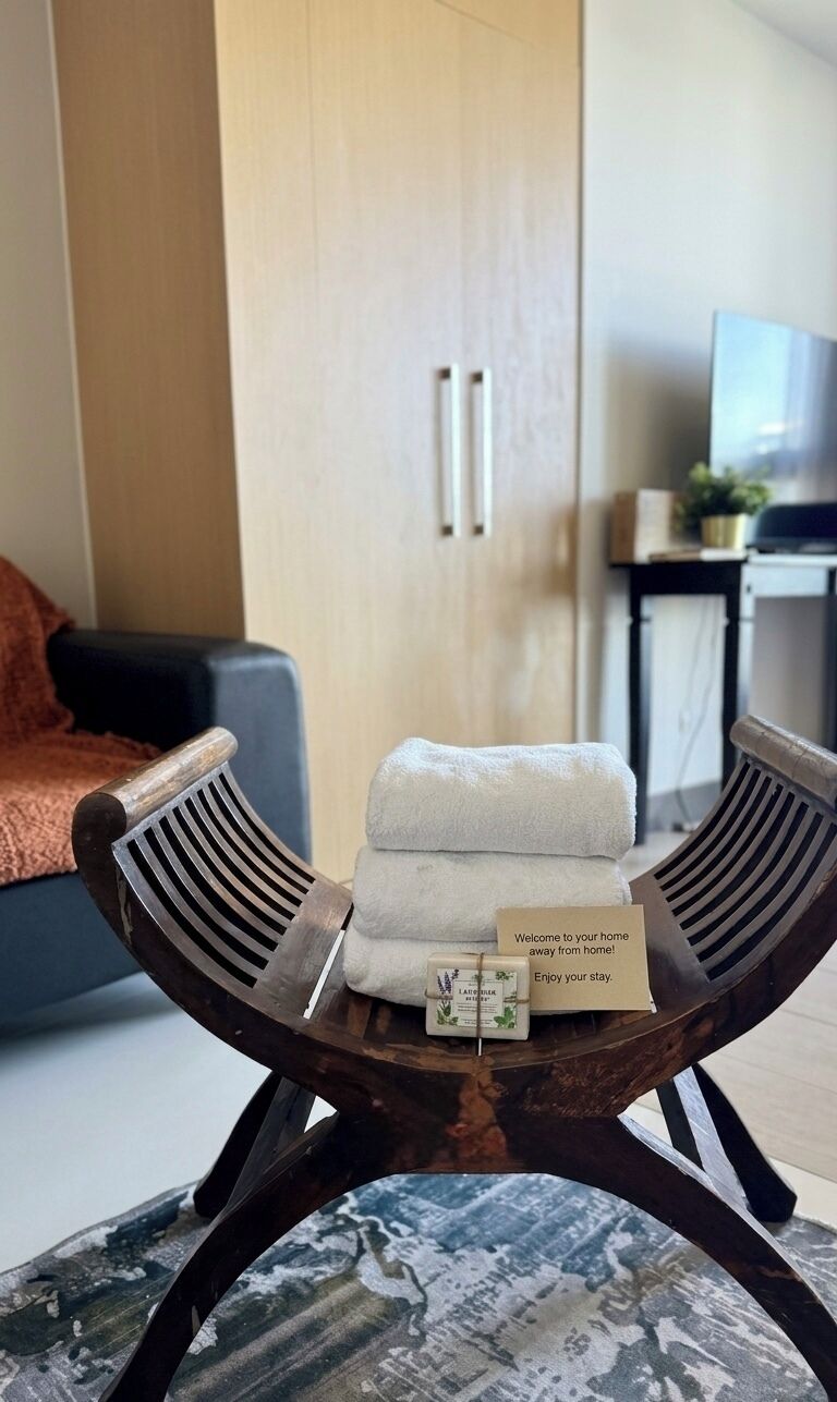 Una habitación moderna con una mesa de madera, una toalla blanca doblada y una tarjeta de bienvenida.