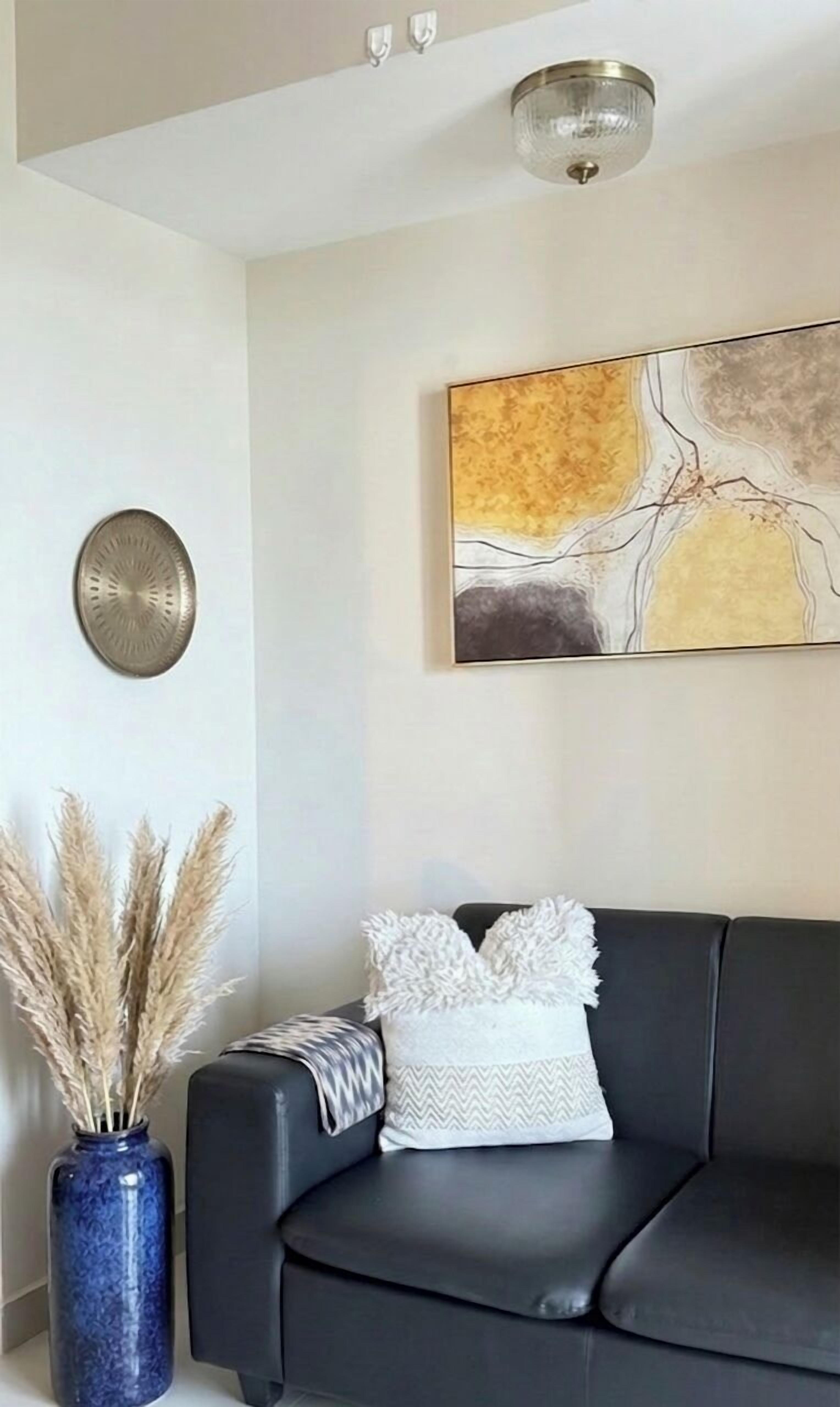 Un soggiorno moderno con un divano in pelle nera, un vaso decorativo con pampas e un quadro astratto contemporaneo appeso al muro.