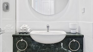 Ein Badezimmer mit einem weißen Waschbecken, einem runden Spiegel und einer Marmorarbeitsplatte.