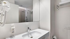 A modern bathroom with a white sink, a mirror, a handheld showerhead, and a towel rack. - B&B HOTEL Sevilla Bormujos (Bormujos)