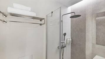 Un espace douche moderne doté d’une porte en verre, d’un pommeau de douche à main et d’un porte-serviettes avec des serviettes pliées.