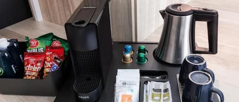 A kitchen area with a coffee maker, kettle, and coffee cups on a tray.